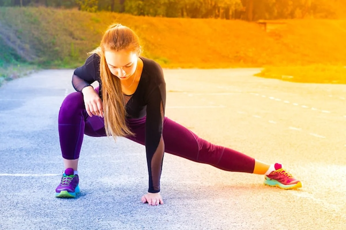 Młoda dziewczyna rozciąga nogi na stadionie przed biegiem