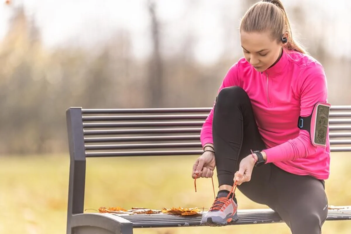 Młoda kobieta w odzieży sportowej wiąże buty na ławce w parku
