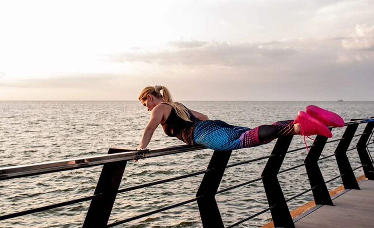 Młoda kobieta robi ćwiczenia sportowe o świcie przy oceanie