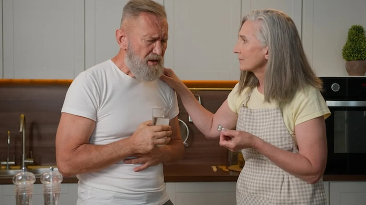 Kobieta pomaga mężczyźnie w kuchni podając lekarstwo